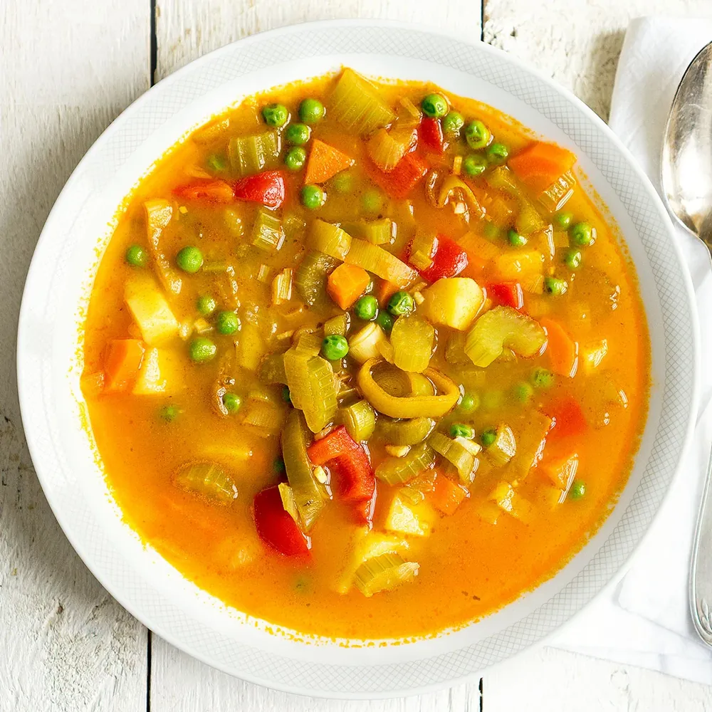 Bunte Gemüsesuppe mit Erbsen, Karotten und Sellerie — Top-down auf weißem Holz